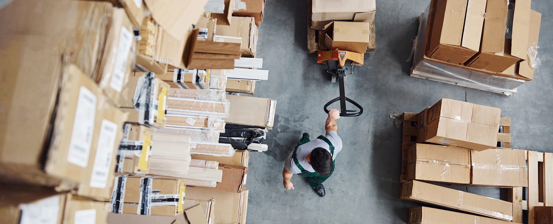 Warehouse worker moving pallet of boxes with pallet jack from above