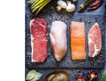 Cuts of meat, chicken, salmon and pork on table top cutting board