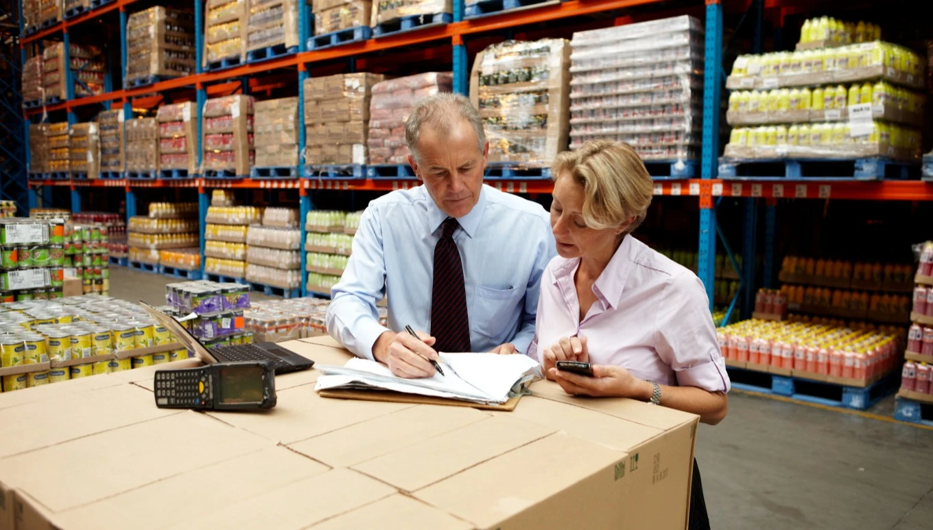 Two food supply chain professionals review documents in the warehouse.