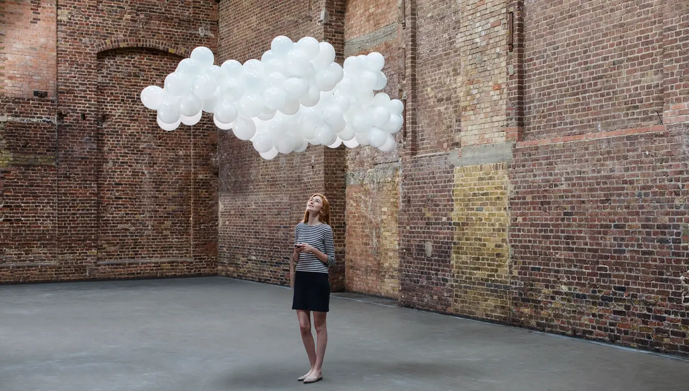 Woman standing looking at white balloons floating like a cloud.