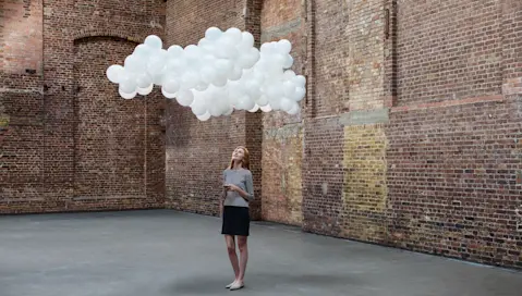 Woman standing looking at white balloons floating like a cloud.