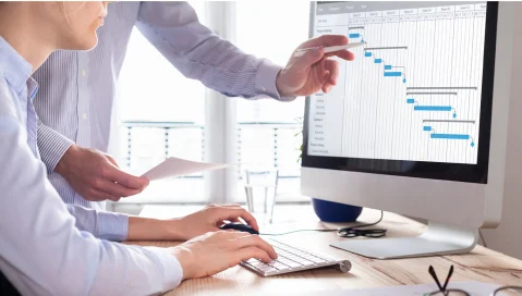 Two men discussing charts on a desktop computer