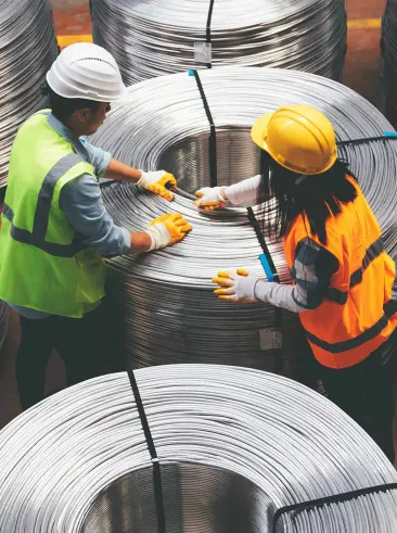Dos trabajadores del metal empaquetando bobinas de cable metálico.