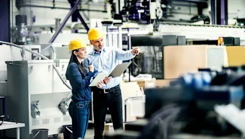 Engineers at an industrial manufacturing plant confer over documents.