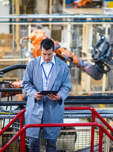 Man in front of robotic arm in factory with tablet.