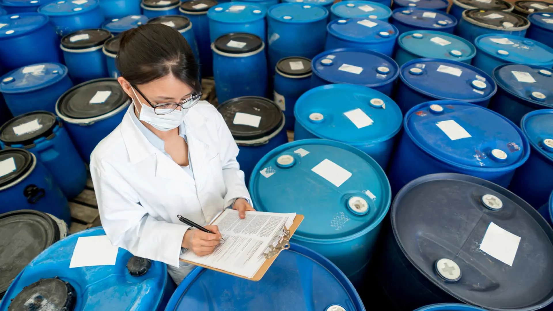 Woman with lab coat on chemical floor taking inventory.