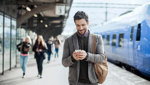 Businessman smiling looking on mobile phone at train station