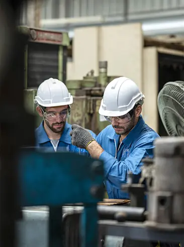 Zwei Fabrikarbeiter mit Schutzhelmen bei der Arbeit.