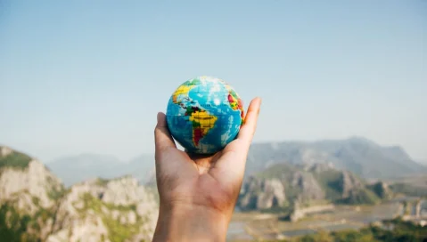A hand holds a small globe with mountains in the background.