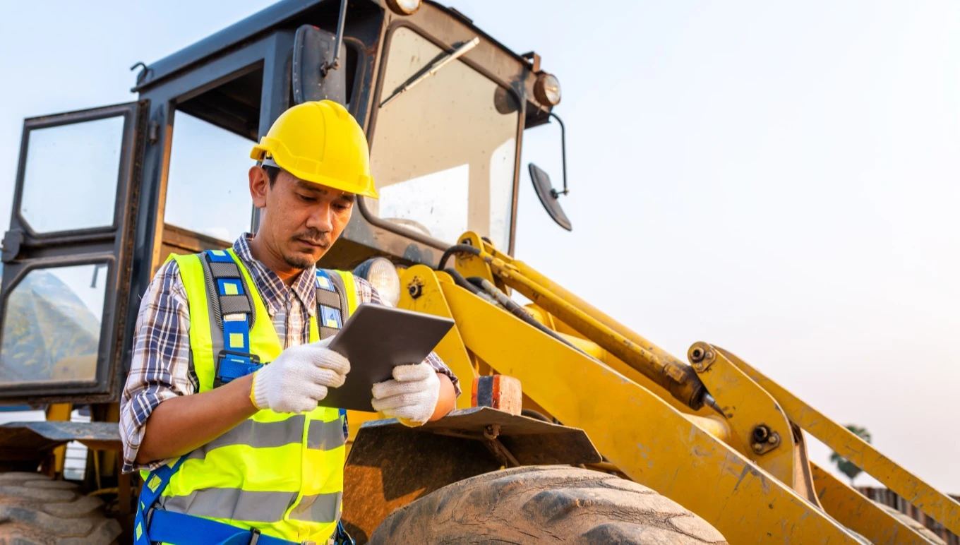 Worker using tablet in front of heavy machinery
