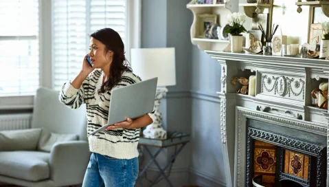 Woman using phone while holding laptop