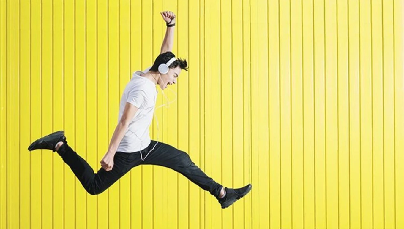 Young man jumping while listening to music through his white headphones.