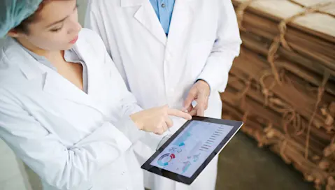 Two food facility workers use business software on a tablet.