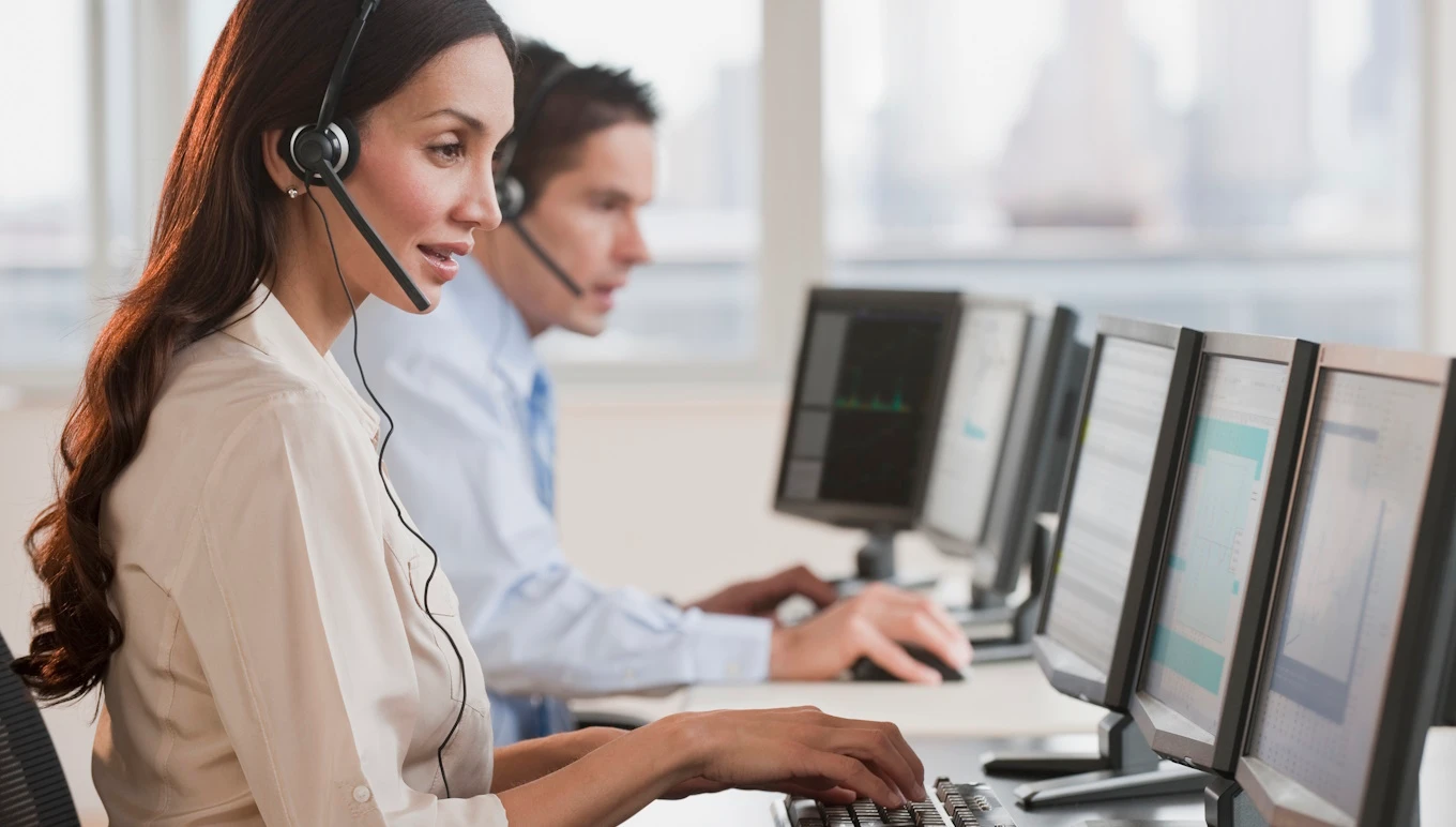 Woman and man wearing headphones and sitting in front of computer screens.