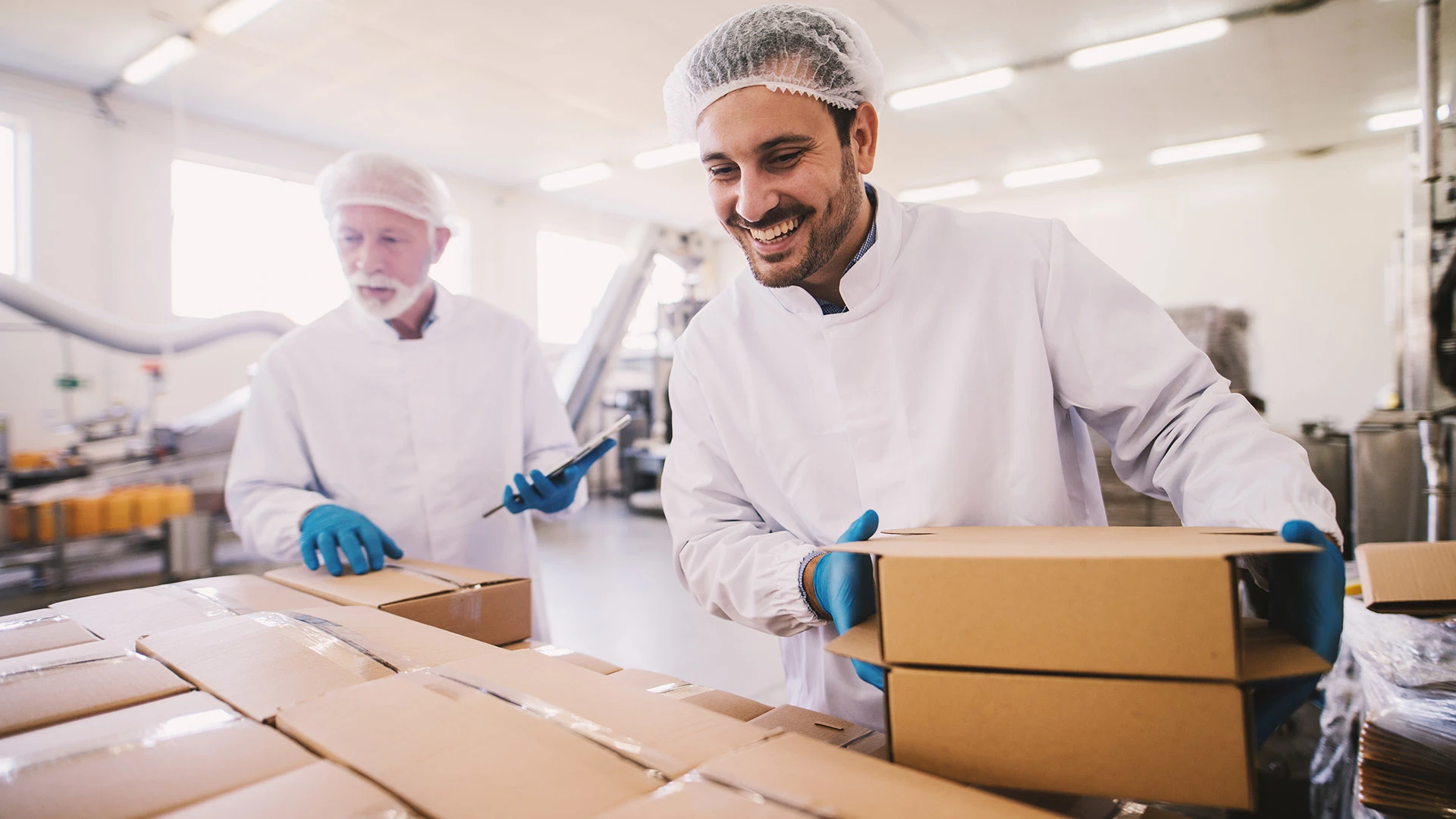 Two men holding boxes in a factory.