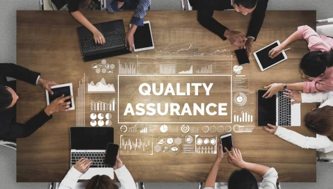 aerial of people working around desk with quality assurance text