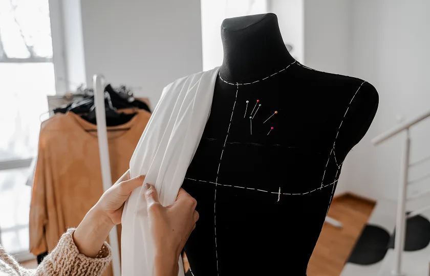 A woman laying fabric over a dress form.