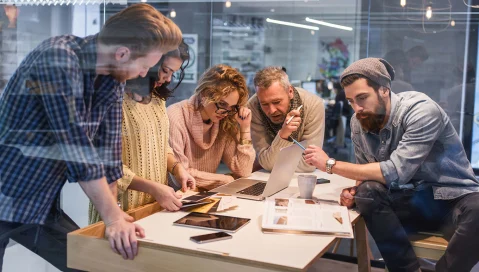 Group of individuals having a meeting looking at a laptop.