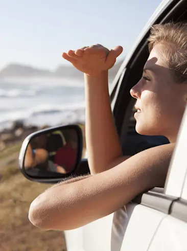 Vrouw tuurt naar oceaan vanuit autodeur op strand.