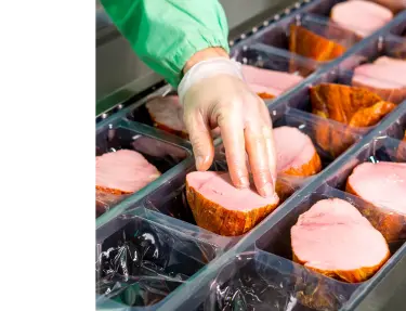 Food factory working handling meat products for packaging.