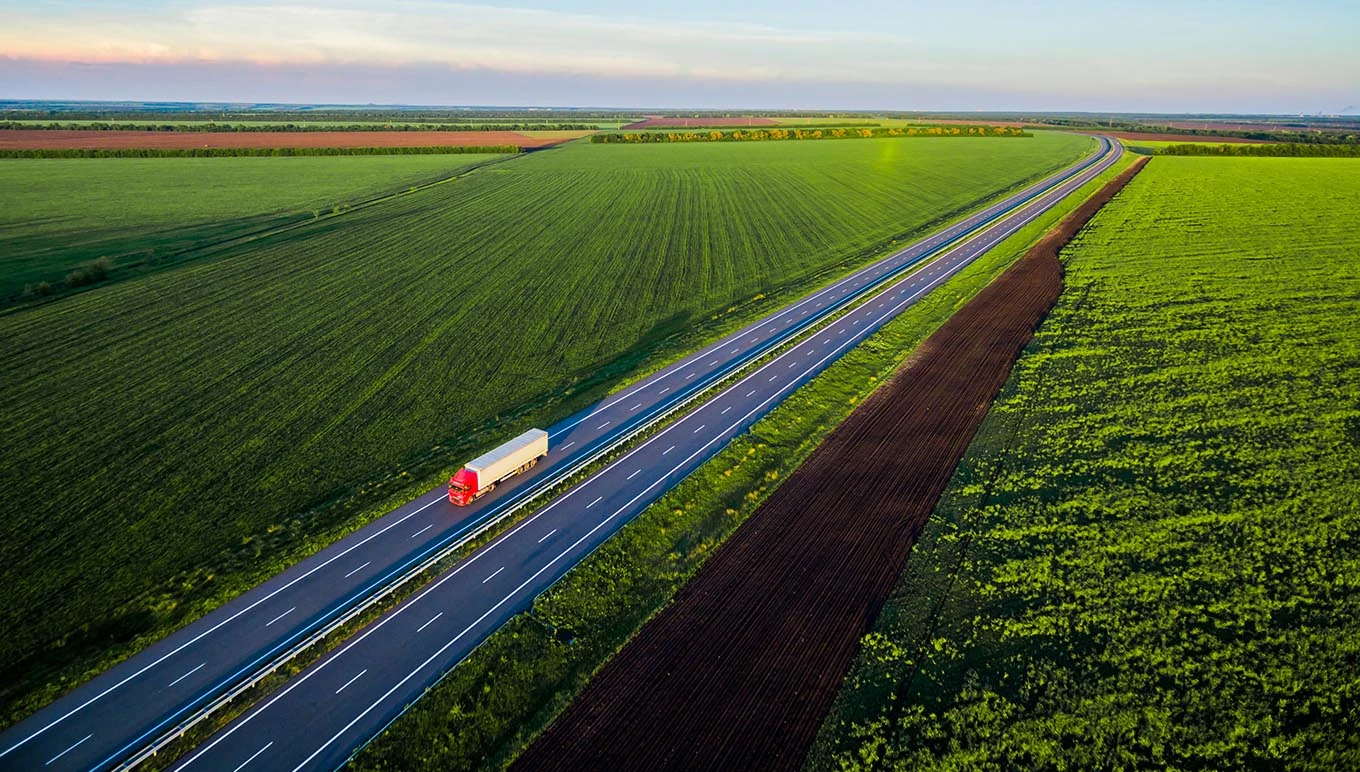 Truck driving on divided highway with green scenic fields on either side.