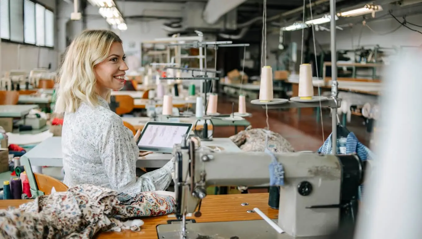 Woman in sewing room sitting with tablet.