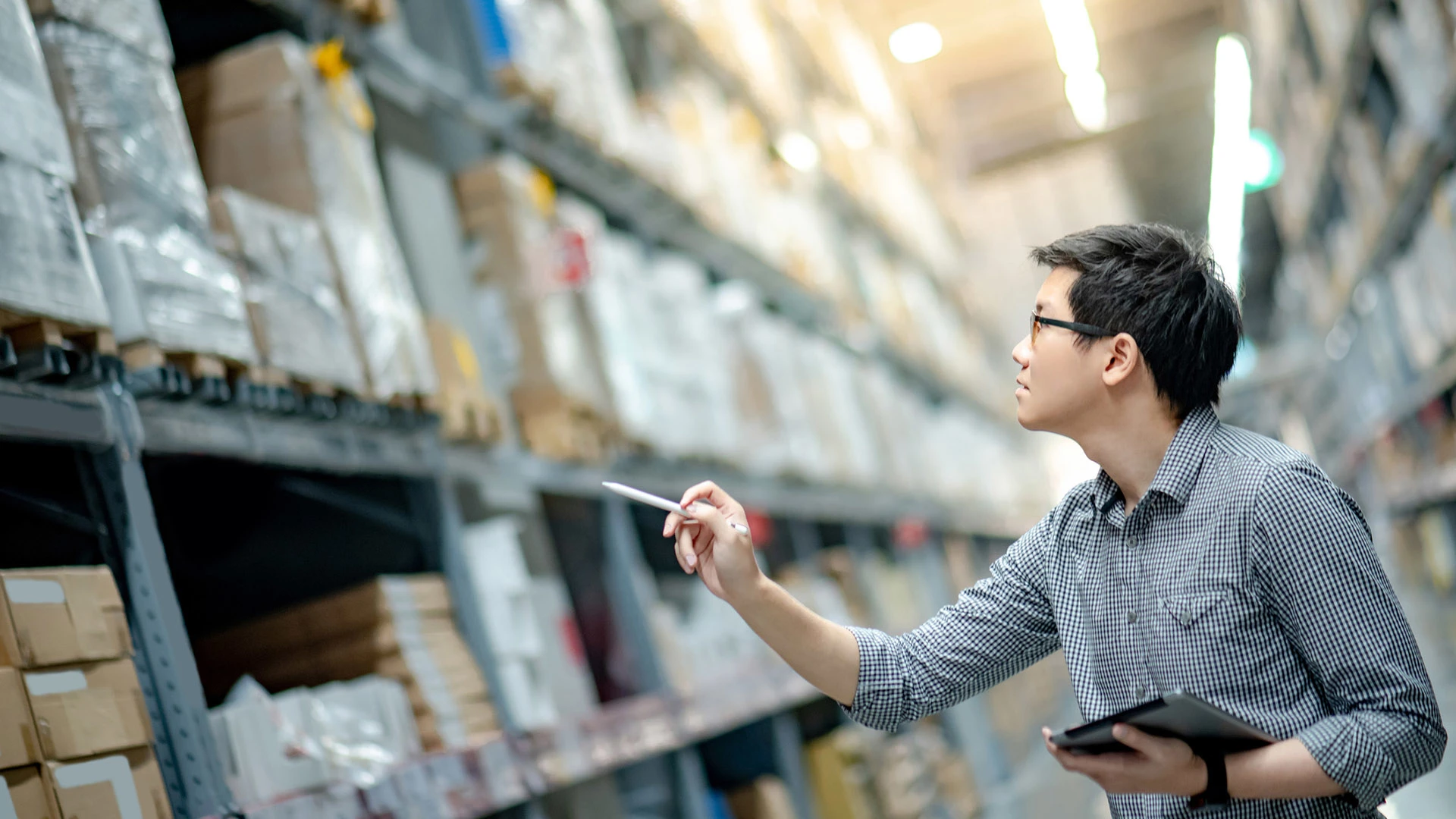 Un homme regarde les stocks dans une usine en tenant une tablette.