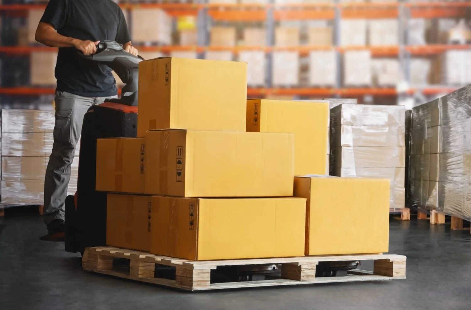 Warehouse worker transporting pallet of boxes with pallet jack