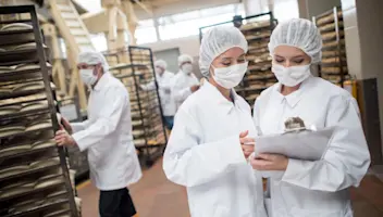 Two masked food facility workers review food related records.