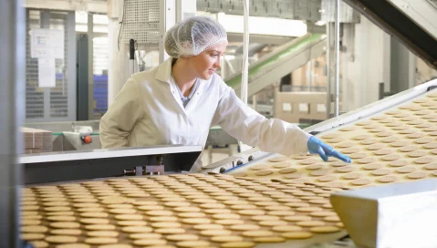 A food facility worker inspects cookies coming off the line.