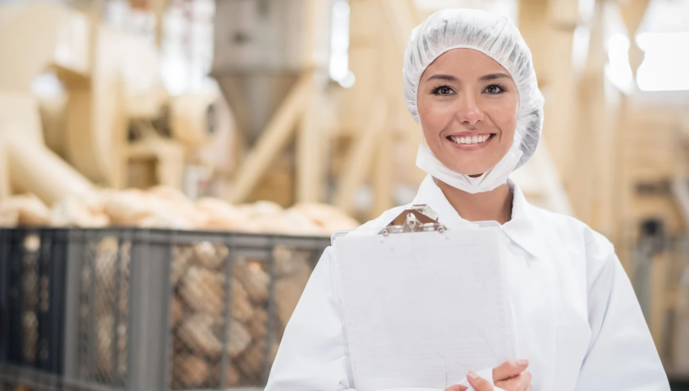 A food facility worker holding a clipboard smiles.