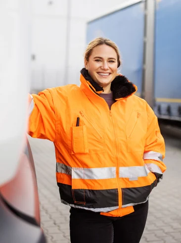 Woman wearing safety jacket near truck depot