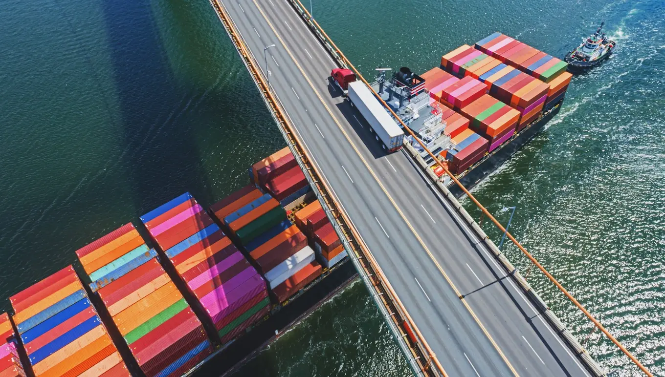 Container ship sails under a bridge where a truck is driving.