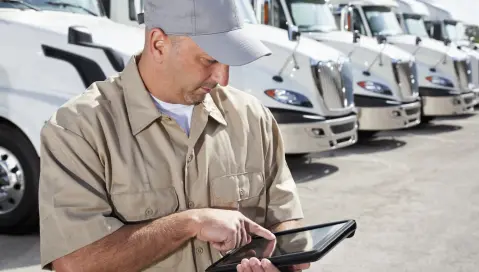 Man looking at tablet in front of trucks.