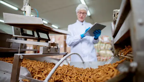 A food factory worker observes manufacturing equipment producing snacks.