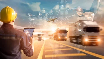 man in hardhat with tablet beside oncoming semitrucks