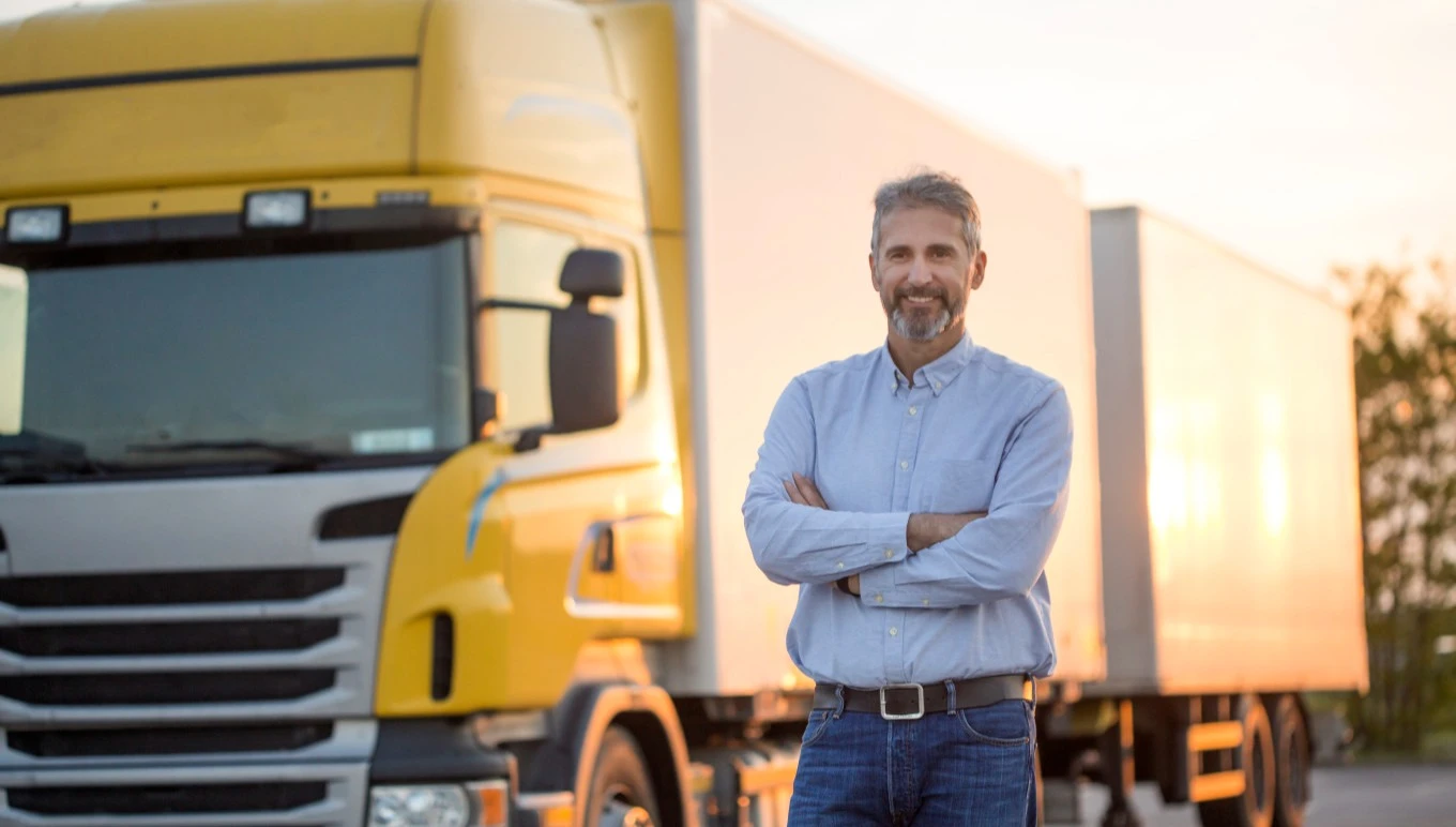 Man standing near delivery fleet truck smiling with arms crossed.