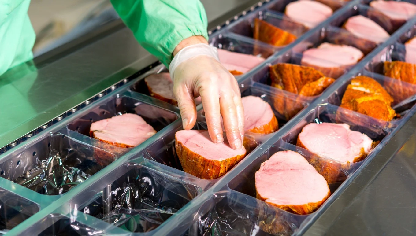 Cuts of ham being packed at a food facility.