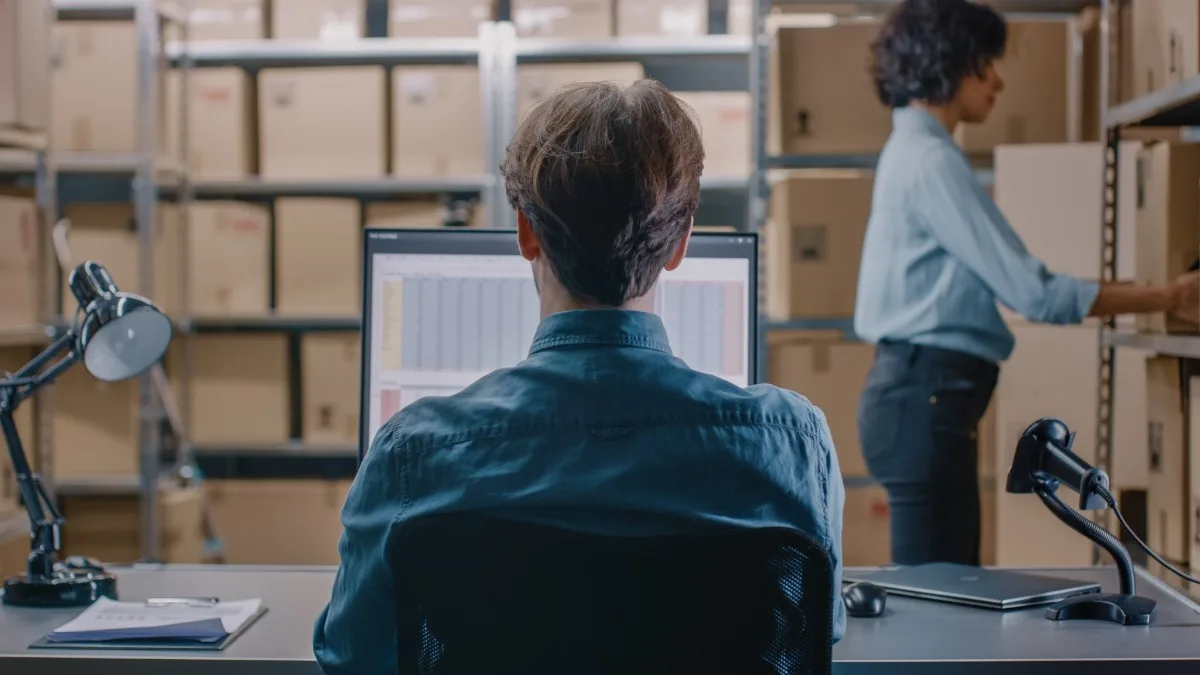 Warehouse staff managing inventory on computer with storage shelves in background