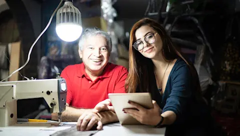 Man and woman in small office with sewing machine and tablet