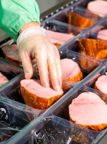 Gloved hand putting ham into plastic pockets