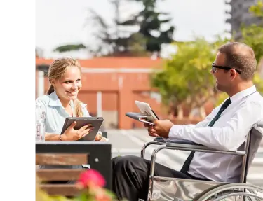 Woman on tablet talking to man with tablet in wheelchair.