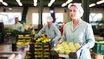 A food facility worker carries a box of fresh fruit.