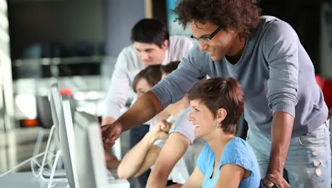 Man pointing something out on a desktop to a lady.