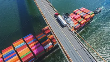 Cargo vessel pushed by tug boat under bridge with truck transport