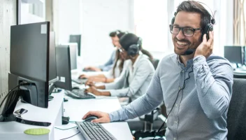 Man smiling wearing a headset using a desktop.