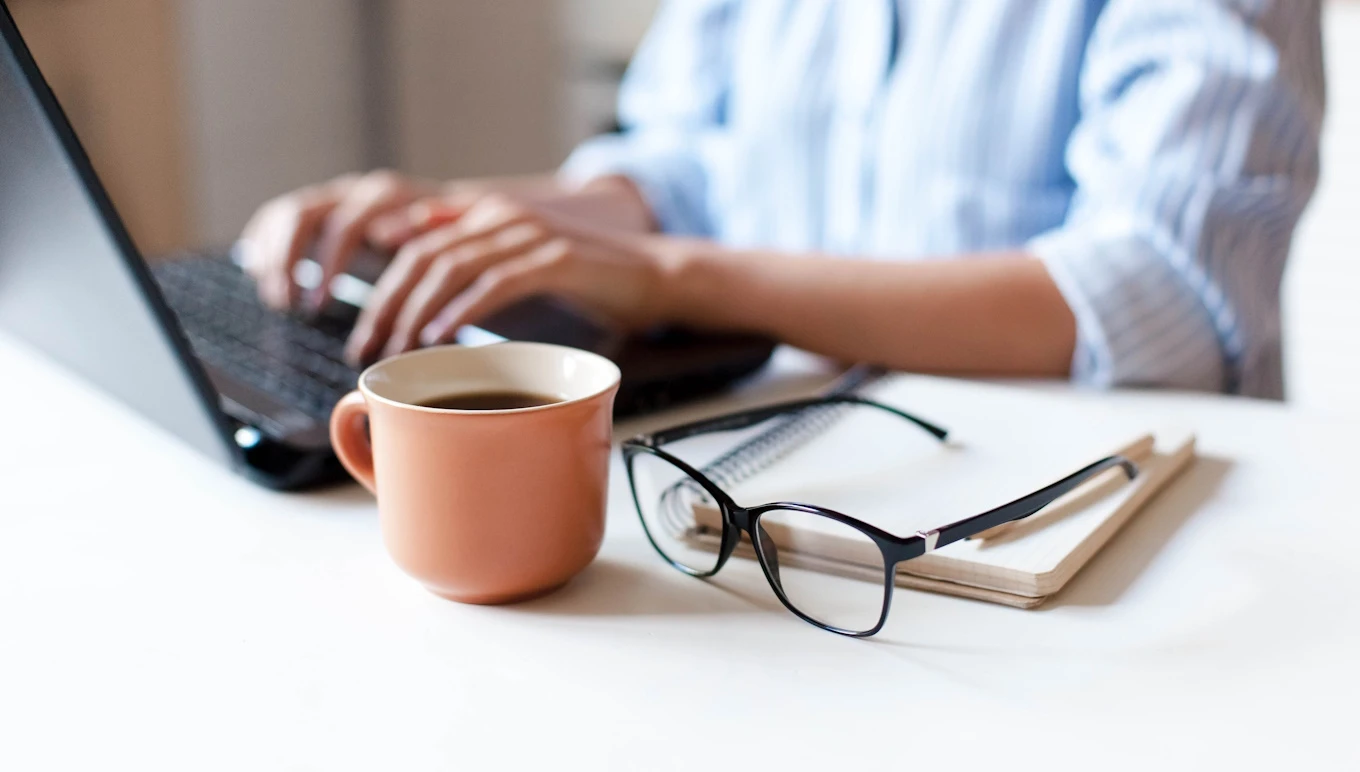 Woman closeup sitting at table with coffee, glasses and computer.