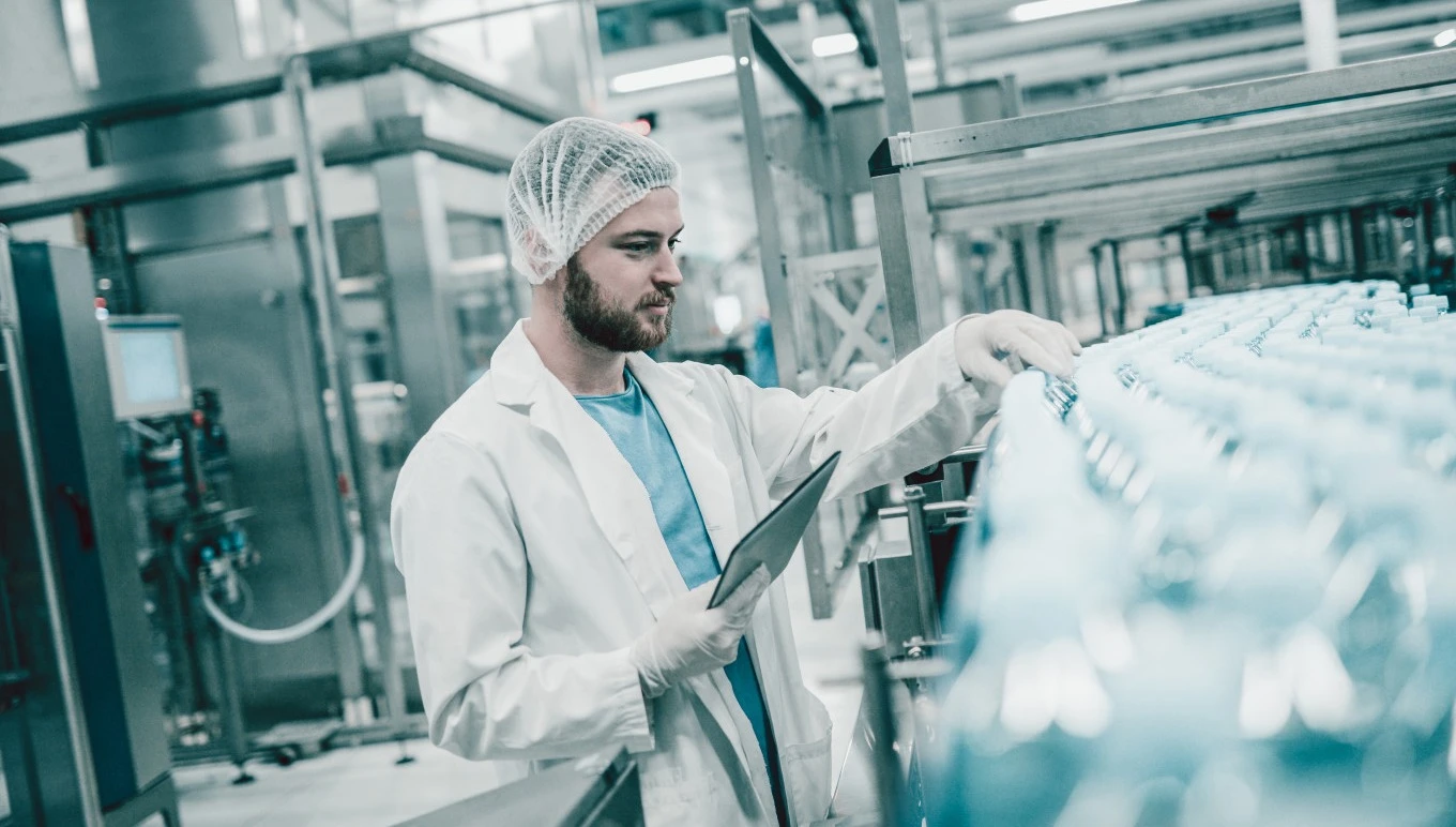 A process manufacturing worker inspects bottles moving along a line.