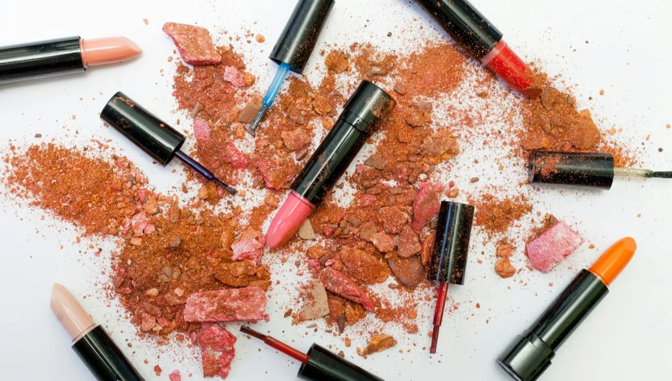 Lipsticks, eyeliners and other powdered cosmetics are strewn across a surface.