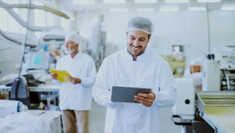 A smiling, confident food manufacturing worker uses software from the floor via tablet.